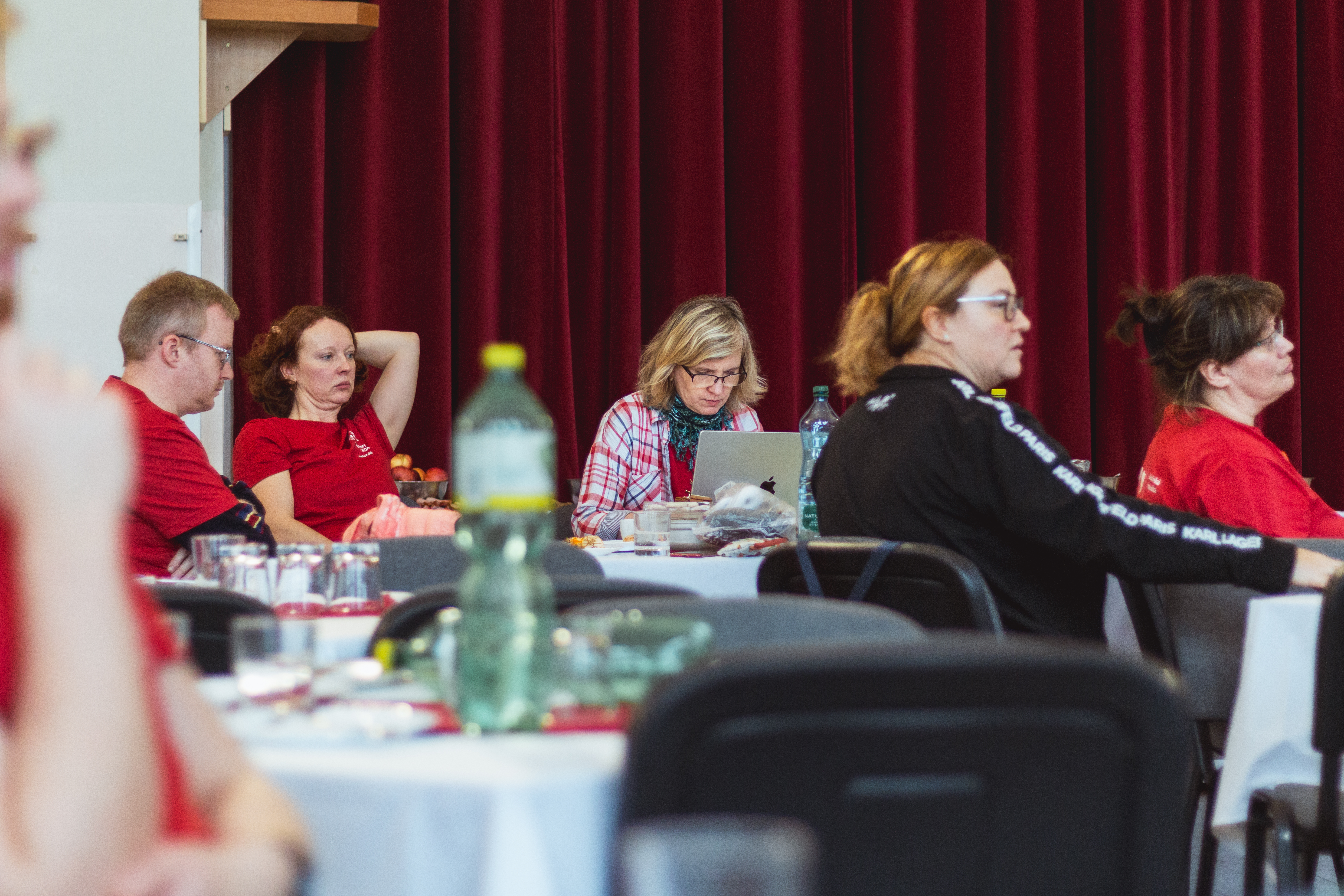 Účastníci u stolů, workshop atmosféra, červený závěs